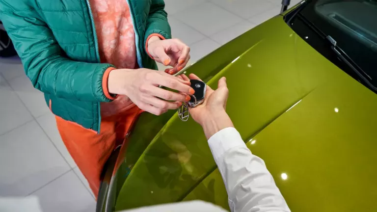 Person übergibt Autoschlüssel an andere Person über Motorhaube eines grünen Autos