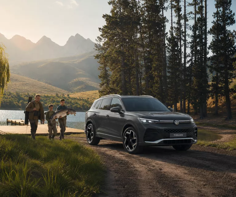 VW Tiguan in grau in der Natur vor einem See mit einer Familie.