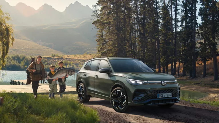 VW Tiguan in grün in der Natur vor einem See mit einer Familie.