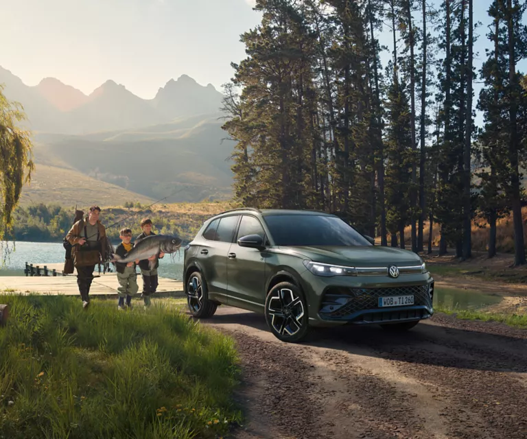 VW Tiguan in grün in der Natur vor einem See mit einer Familie.
