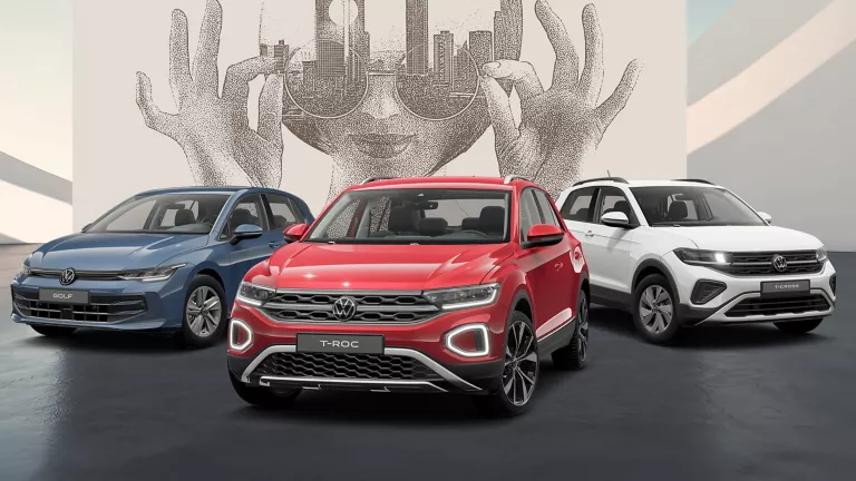 Drei VW Modelle in blau, rot und weiß auf schwarzem Boden vor einer Wand mit abstrakter Kunst.