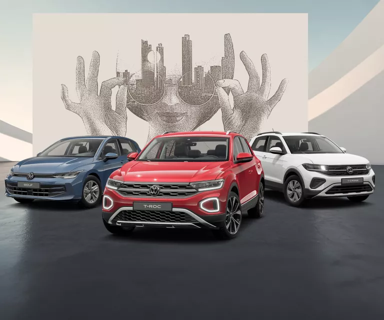 Drei VW Modelle in blau, rot und weiß auf schwarzem Boden vor einer Wand mit abstrakter Kunst.