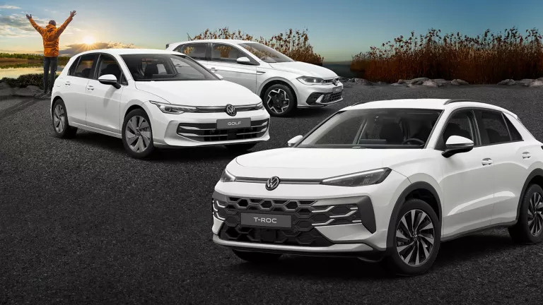 Drei VW-Modelle stehen auf Asphalt, vor Schilf und einem See.