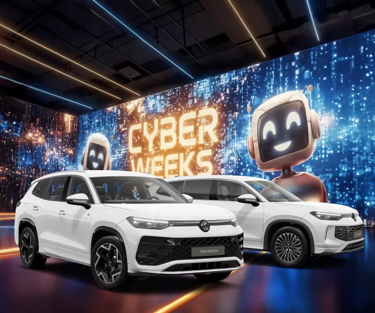 Zwei VW Tayrons vor einer großen digitalen Wand mit leuchtendem Schriftzug "CYBER WEEKS" und zwei lächelnden Roboter.