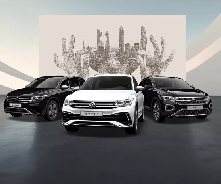 Seitliche Ansicht eines T-Roc und eines Tiguan auf schwarzem Boden vor einer Wand mit abstrakter Kunst.