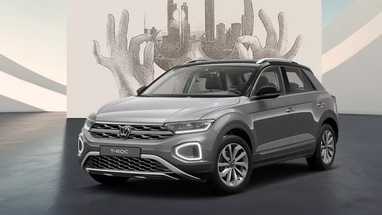 Seitlich frontale Ansicht eines grauen VW T-Roc auf schwarzem Boden vor einer Wand mit abstrakter Kunst.