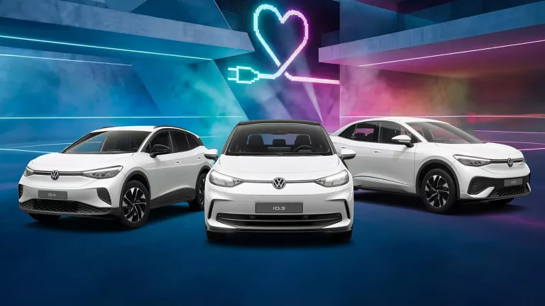 Drei VW Modelle vor Gebäude mit bunten LED's, im Hintergrund Herzsymbol mit Ladekabel-Stecker