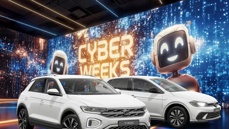 Zwei VW-Modelle vor einer großen digitalen Wand mit leuchtendem Schriftzug "CYBER WEEKS" und zwei lächelnden Roboter.