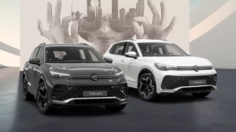 Seitliche Ansicht von Zwei VW Tiguans in Weiß und Grau auf schwarzem Boden vor einer Wand mit abstrakter Kunst.