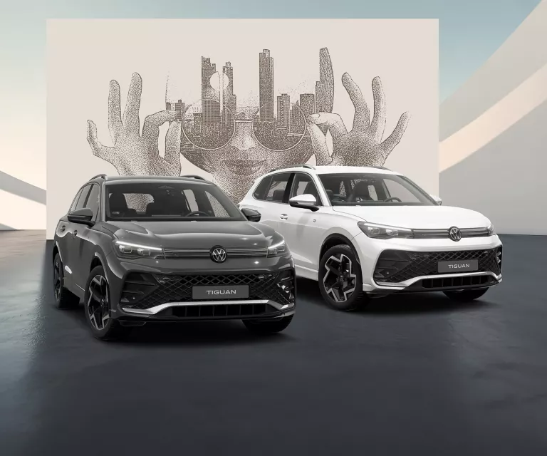 Seitliche Ansicht von Zwei VW Tiguans in Weiß und Grau auf schwarzem Boden vor einer Wand mit abstrakter Kunst.