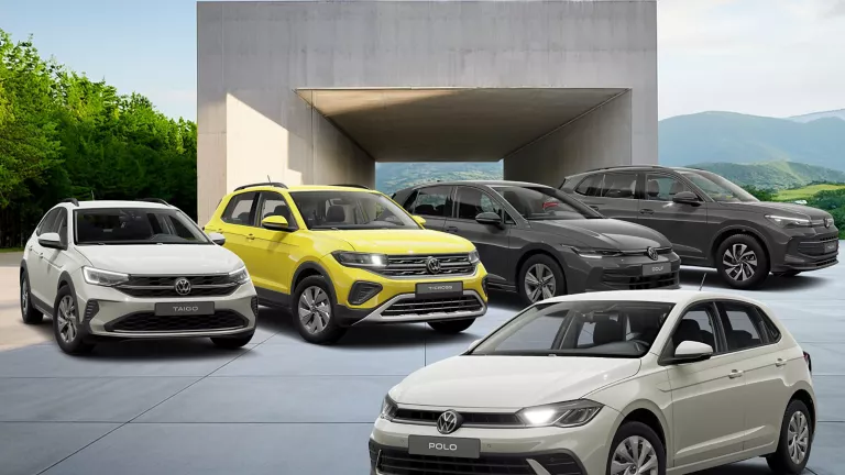 Fünf VW-Modelle auf einem gepflasterten UNtergrund, Im Hintergrundein Beton Gebäude, berge und blauer Himmel