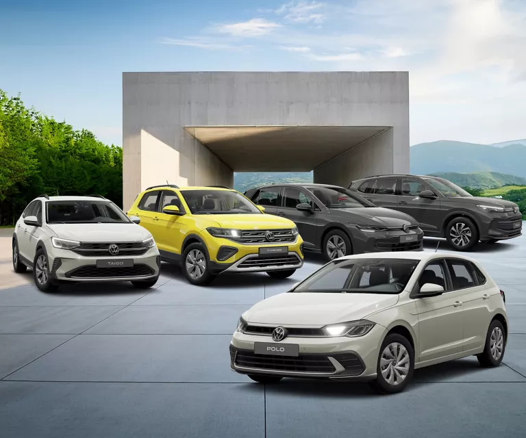 Fünf VW-Modelle auf einem gepflasterten UNtergrund, Im Hintergrundein Beton Gebäude, berge und blauer Himmel