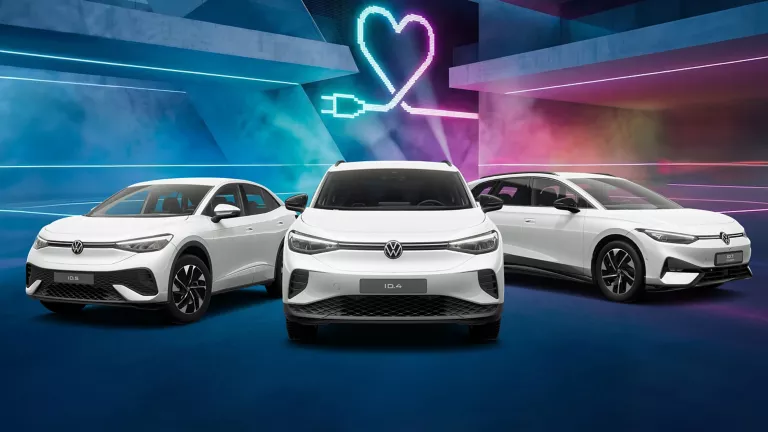 Drei VW Modelle vor Gebäude mit bunten LED's, im Hintergrund Herzsymbol mit Ladekabel-Stecker