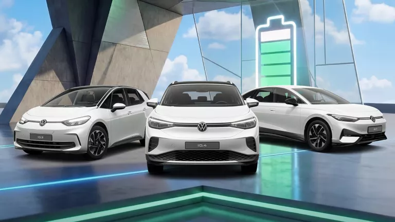 Drei VW Modelle vor Gebäude mit bunten LED's, im Hintergrund Ladebalken