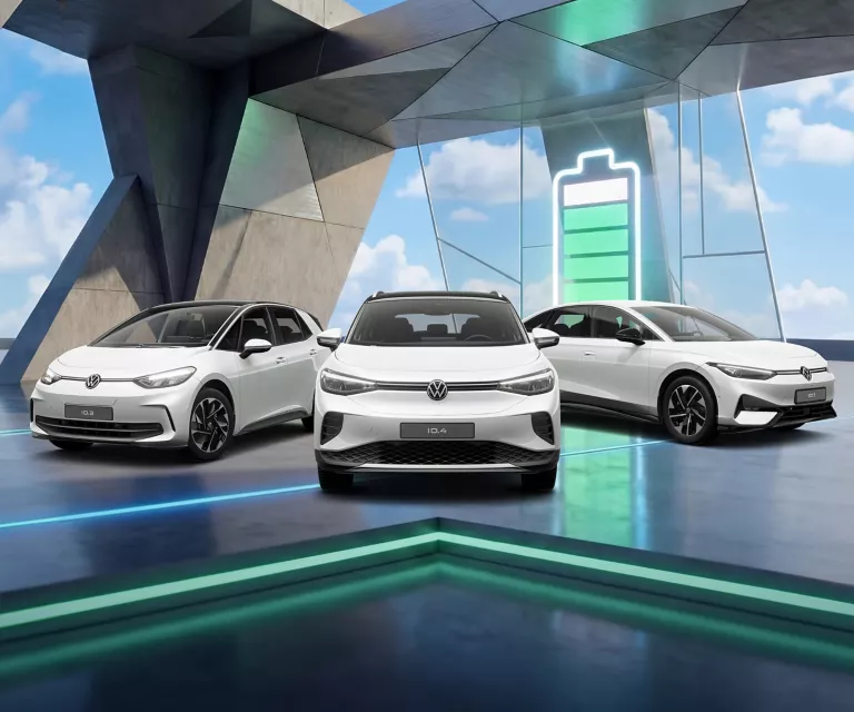 Drei VW Modelle vor Gebäude mit bunten LED's, im Hintergrund Ladebalken