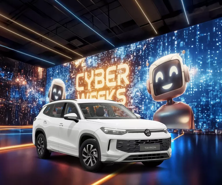 Weißer VW Tayron Life vor einer großen digitalen Wand mit leuchtendem Schriftzug "CYBER WEEKS" und zwei lächelnden Roboter.
