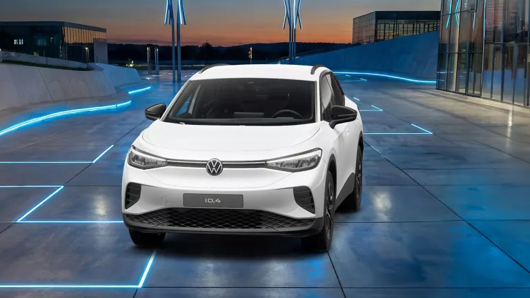 Weißer VW ID.4 auf einem futuristischen Platz mit blauen Leuchtlinien und moderner Architektur im Hintergrund.