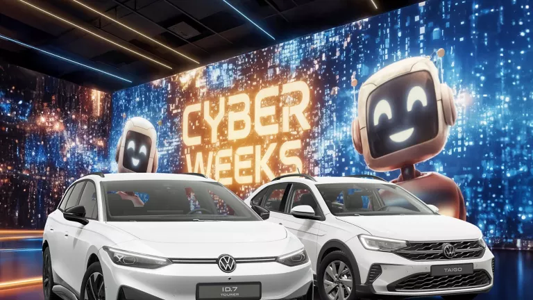 Drei VW-Modelle vor einer großen digitalen Wand mit leuchtendem Schriftzug "CYBER WEEKS" und zwei lächelnden Roboter.