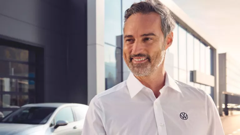 Ein Serviceberater übergibt einer Kundin vor dem Autohaus ihren Autoschlüssel.