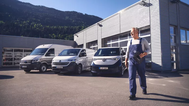 VW Service Mitarbeiter vor einer Reihe von VW Nutzfahrzeugen.