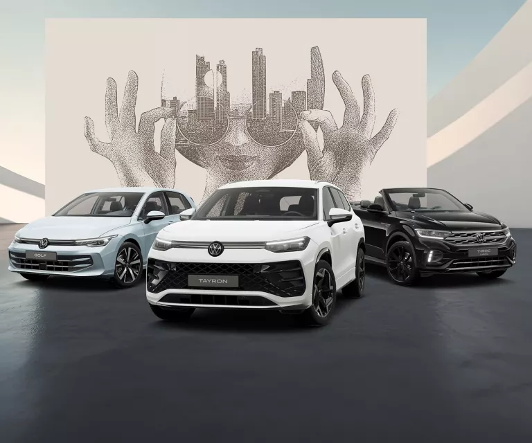 Drei VW Modelle in blau und weiß stehen auf schwarzem Boden vor einer Wand mit abstrakter Kunst.