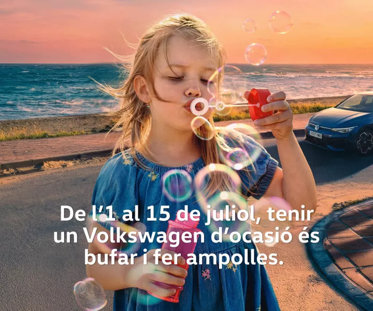 Una nena bufan unes ampollas amb un Volkswagen blau a la platja