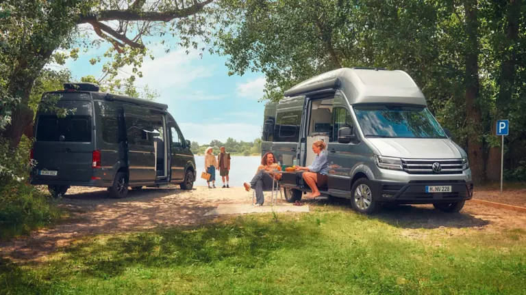 Zwei Pärchen und ihre VW California in einer idyllischen Seenlandschaft.