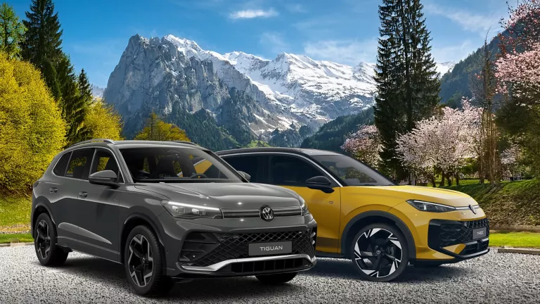 Ein VW Tiguan und ein V T-Roc parken auf einem Parkplatz. Im Hintergrund sieht man ein herrliches Berg Panorama.