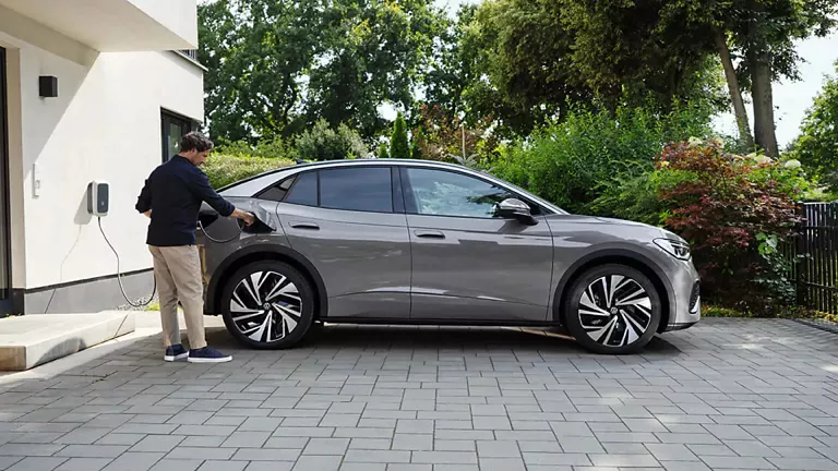 Un hombre cargando un Volkswagen ID.5 gris junto a su casa