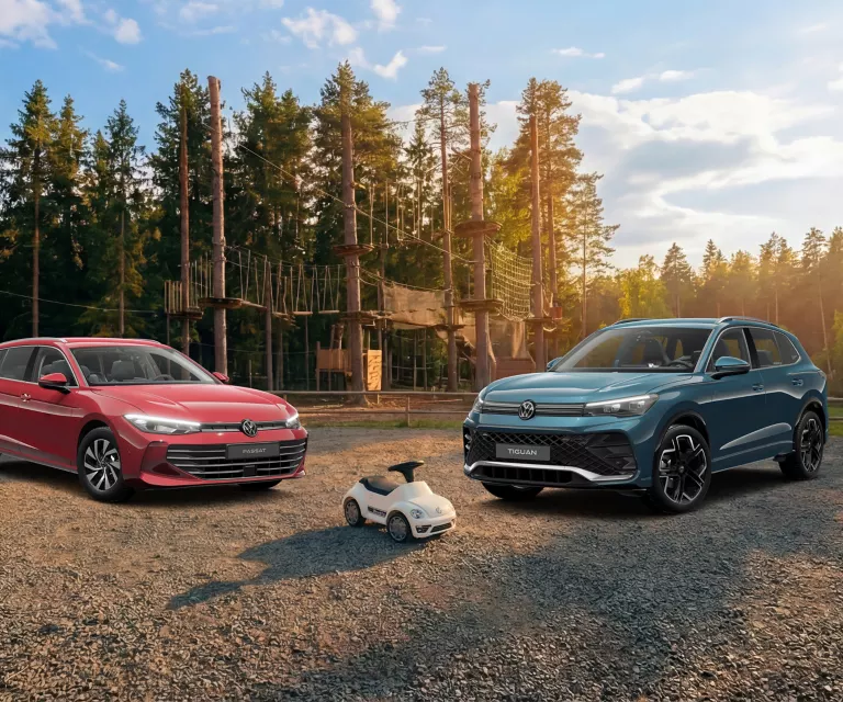 Zwei VW Modelle stehen auf einem Schotterplatz vor einem Wald-Kletterpark, zwischen ihnen ein kleines VW Spielzeugauto.
