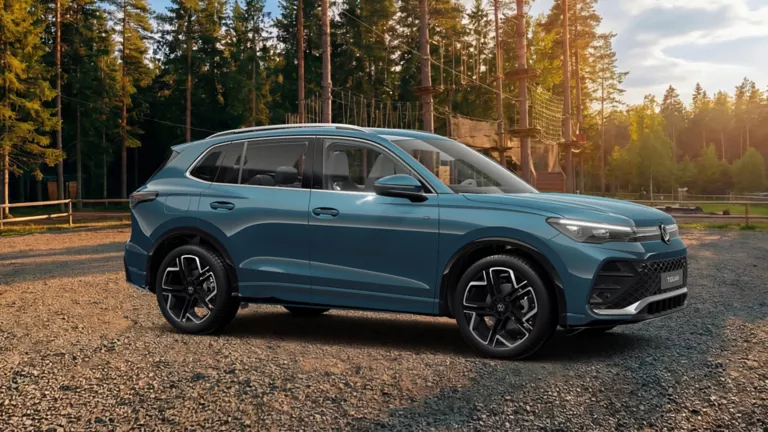 Seitenansicht auf eines blauen VW Tiguan auf einem Schotterplatz vor einem Wald-Kletterpark.