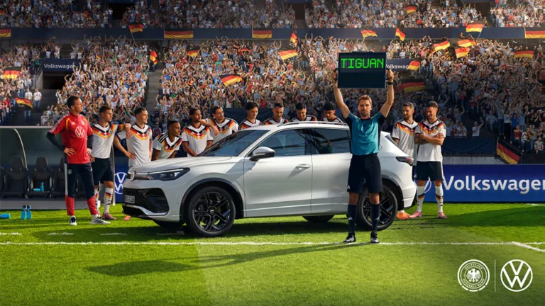 Ein weißer Tiguan R-Line steht mit der Herren Fußballnationalmannschaft auf einer Rasenfläche im Stadion. Der Schiedsrichter hält die Wechselanzeige mit dem Schriftzug „Tiguan“ in die Höhe.