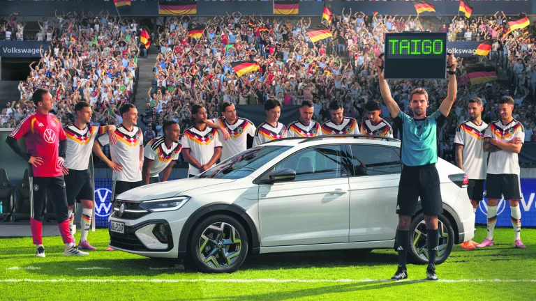 VW Taigo auf einem Fussballfeld, Schiedsrichter hält ein Leuchtschild mit der Aufschrift "Taigo" hoch