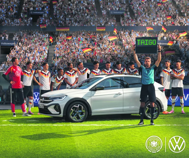 VW Taigo auf einem Fussballfeld, Schiedsrichter hält ein Leuchtschild mit der Aufschrift "Taigo" hoch