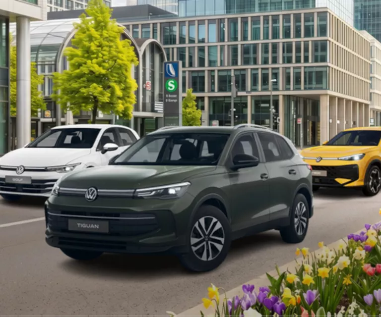Ein weißer VW Golf, ein gelber VW T-Roc & ein grauer VW Tiguan stehen in einer urbanen Straße umgeben von blühenden Blumen.