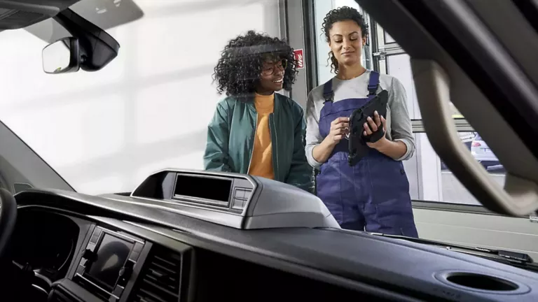 Ein Mechanikerin und eine Kundin unterhalten sich über die Windschutzscheibe eines Fahrzeugs.