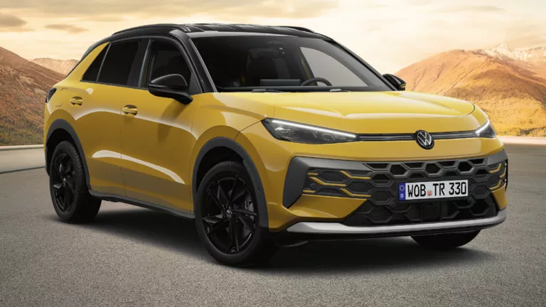 Gelber VW T-Roc auf einer leeren Bergstraße mit sanften Hügeln und Bergen im warmen Abendlicht, ausgezeichnet als „Gewinner 2025 – Das Goldene Lenkrad“.