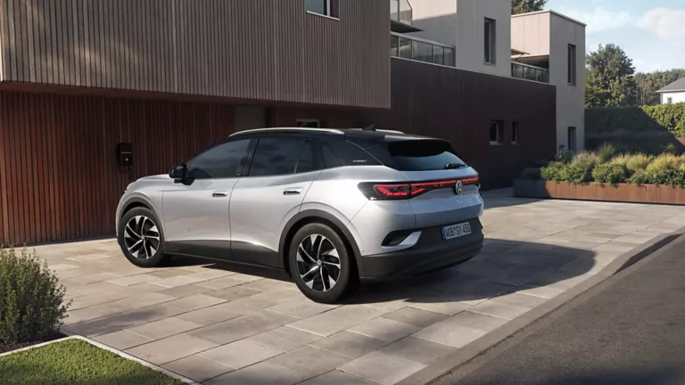  Silberner Volkswagen ID.4 Elektro-SUV von hinten rechts geparkt vor modernem Wohnhaus mit Holzfassade