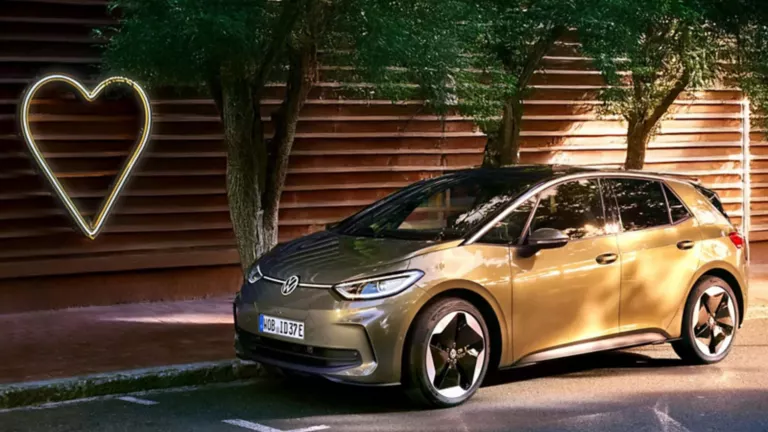 Ein Volkswagen ID.3 steht am Straßenrand unter grünen Bäumen vor einer modernen Holzfassade. Links im Bild leuchtet ein großes Herz-Symbol.