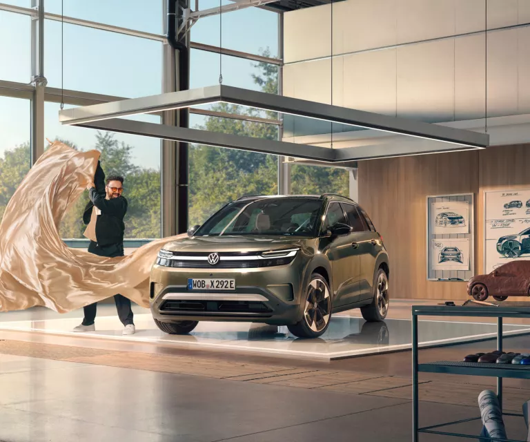 Ein Mann zieht ein großes Tuch von einem grünen VW ID. Cross, der in einem minimalistisch eingerichteten Designstudio steht.
