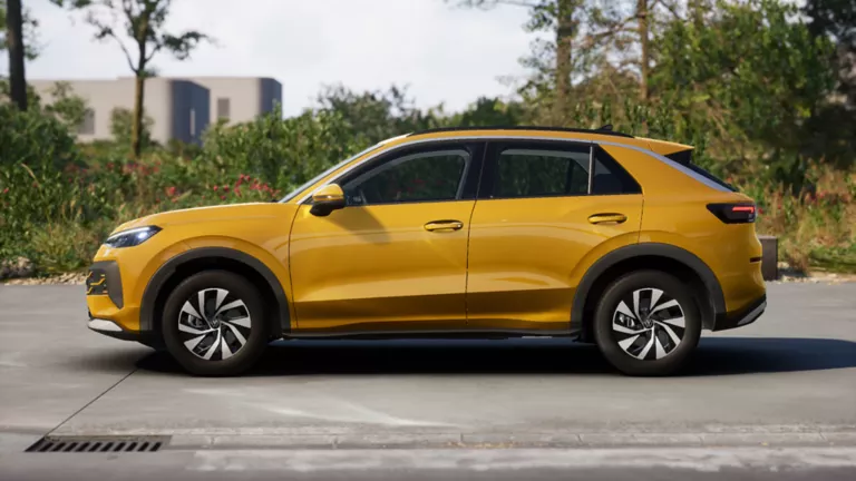 Gelber VW T-Roc SUV, Frontansicht, geparkt auf Asphalt, umgeben von Bäumen und Sträuchern.