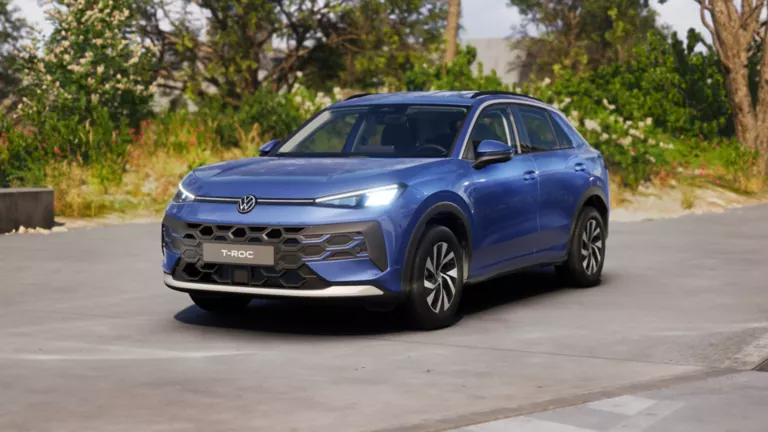 Gelber VW T-Roc SUV, Frontansicht, geparkt auf Asphalt, umgeben von Bäumen und Sträuchern.