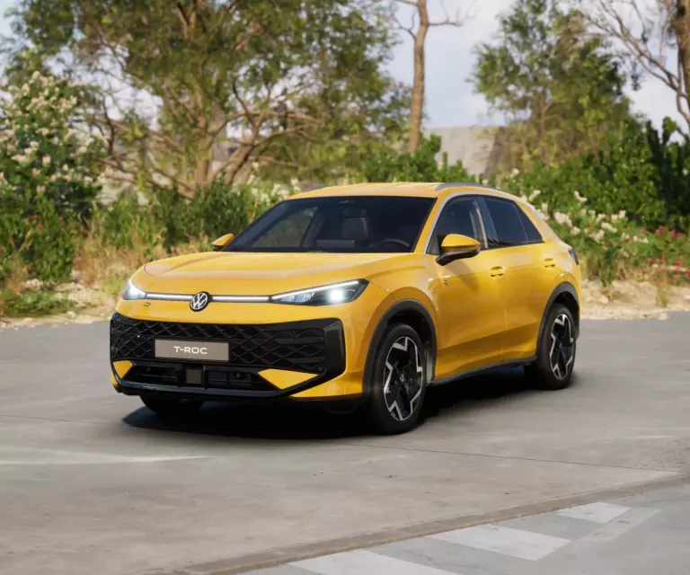 Gelber VW T-Roc SUV, Frontansicht, geparkt auf Asphalt, umgeben von Bäumen und Sträuchern.