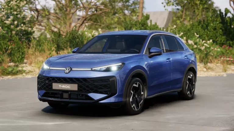 Hellblauer VW T-Roc SUV, Frontansicht, geparkt auf Asphalt, umgeben von Bäumen und Sträuchern.