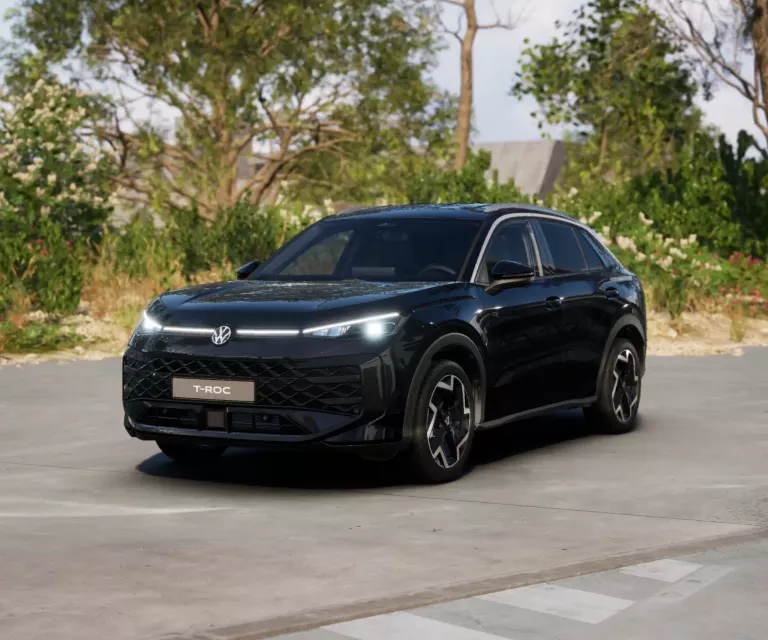 Schwarzer VW T-Roc SUV, Frontansicht, geparkt auf Asphalt, umgeben von Bäumen und Sträuchern.