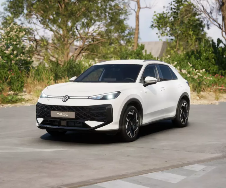 Weißer VW T-Roc SUV, Frontansicht, geparkt auf Asphalt, umgeben von Bäumen und Sträuchern.