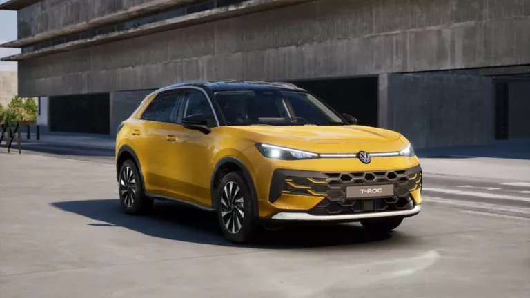 Gelber VW T-Roc SUV, Frontansicht, geparkt auf Asphalt, umgeben von Bäumen und Sträuchern.