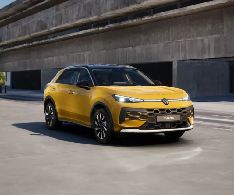 Gelber VW T-Roc SUV, Frontansicht, geparkt auf Asphalt, umgeben von Bäumen und Sträuchern.