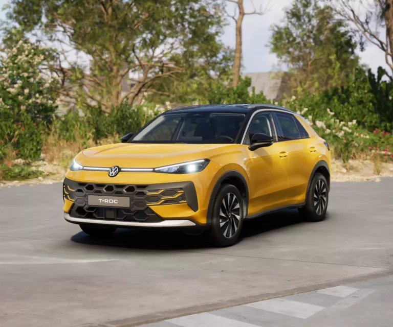 Gelber VW T-Roc SUV, Frontansicht, geparkt auf Asphalt, umgeben von Bäumen und Sträuchern.