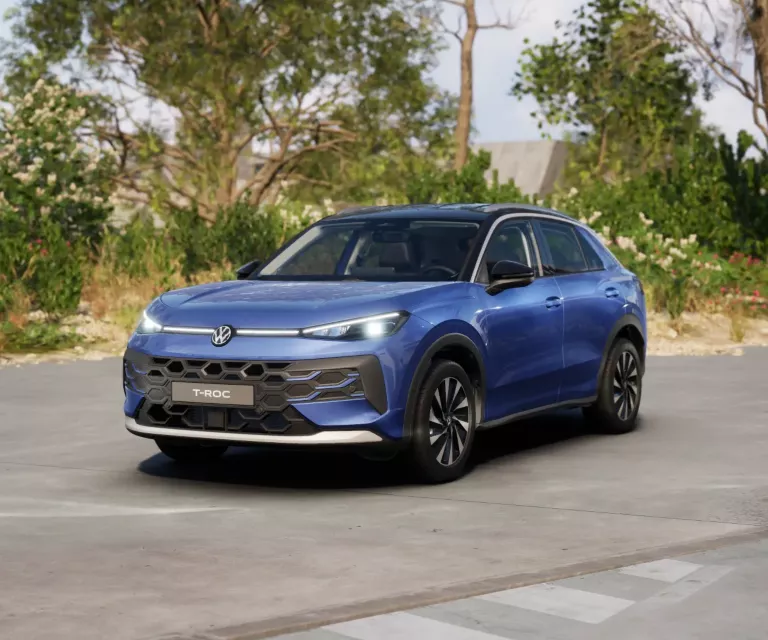 Blauer VW T-Roc SUV, Frontansicht, geparkt auf Asphalt, umgeben von Bäumen und Sträuchern.